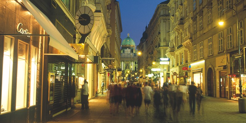 Shopping street in Vienna (Kolhmarkt) leading to historical palace Hofburg during evening with street lights